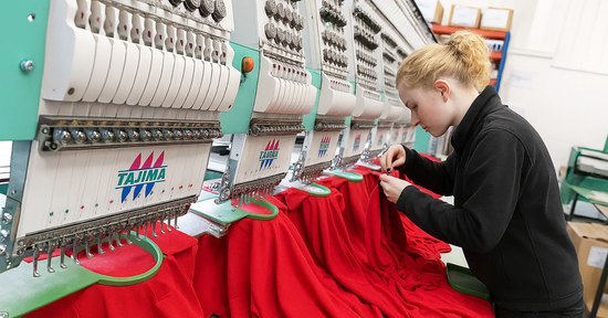 Technician preparing red workwear garments on a Tajima embroidery machine, showcasing high-quality embroidery production in a professional embroidery workshop.