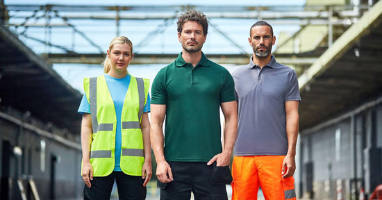Three workers wearing high-visibility and professional workwear, including a hi-vis vest, polo shirts, and safety trousers, standing in an industrial outdoor setting.
