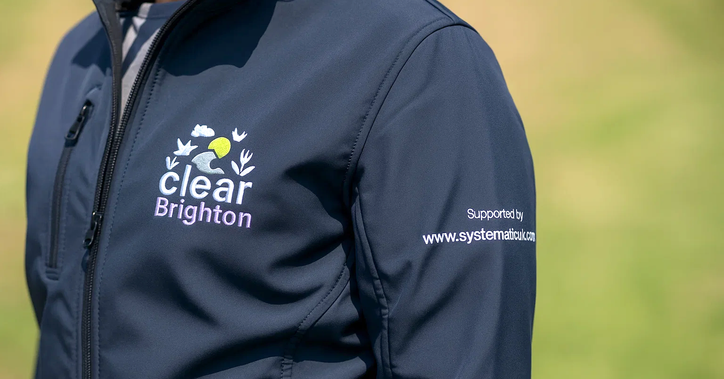 Close-up of a navy softshell jacket featuring detailed embroidered branding for "Clear Brighton" on the chest and a sponsor's website on the sleeve.